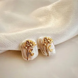 Close-up of baroque pearl earrings with golden flower detail on white silk background