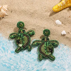 Close-up of hand-woven green beaded sea turtle earrings on a beach-themed backdrop