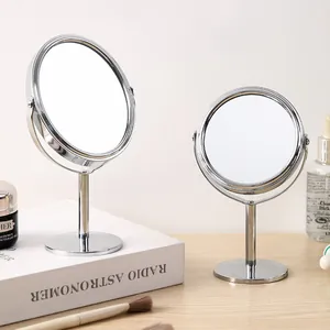 Miroir de maquillage rotatif argenté double face posé sur une table en bois