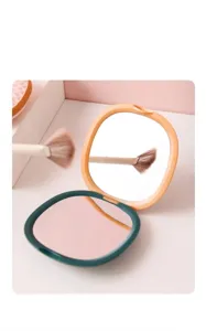 Detail of portable folding makeup mirror in teal and orange with dual-sided design.