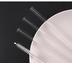 Detail view of three clear borosilicate glass straws with a cleaning brush on a plate