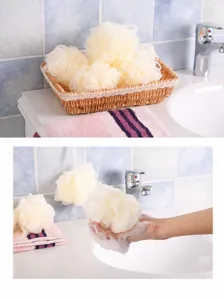 Détail de l'éponge de bain en maille crème tenue à la main avec une mousse de savon riche
