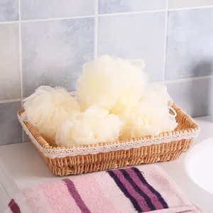 Four cream-colored mesh bath sponges in a woven basket for gentle body exfoliation