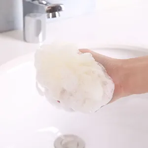 Soft white mesh bath sponge loofah with rich soap foam held by hand over white sink