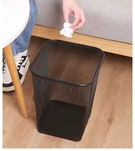 Person throwing waste paper into a black square metal mesh trash can in a home office