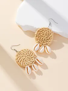 Close-up of handmade round woven rattan earrings with hanging natural white cowrie shells
