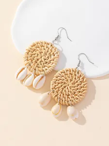 Detail view of handmade woven rattan round earrings with natural cowrie shell drops.