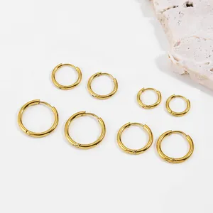 Set of golden stainless steel hoop earrings in various sizes on minimalist background