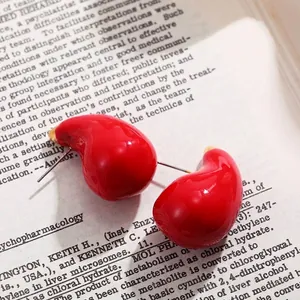 Détail de boucles d'oreilles puces goutte d'eau en émail rouge brillant sur livre