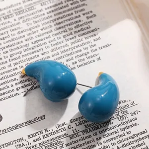 Gros plan détaillé de boucles d'oreilles gouttes d'eau peintes en bleu sarcelle sur livre