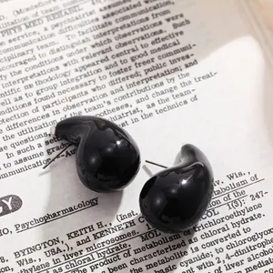 Boucles d'oreilles clous noires brillantes en forme de goutte sur fond de livre.