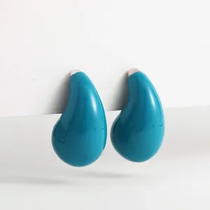 Gros plan d'élégantes boucles d'oreilles puces en émail goutte bleu paon sur fond blanc