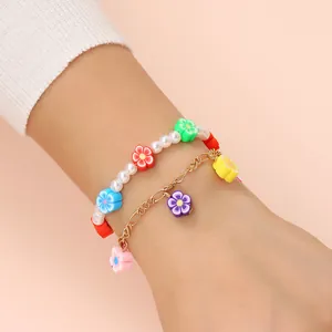 Dettaglio ravvicinato di braccialetti con ciondoli a fiori colorati, perle e catena dorata