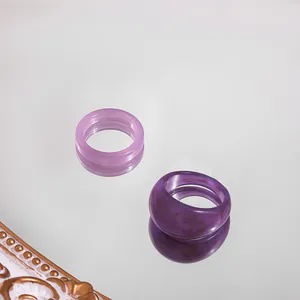Close-up detail view of two trendy purple acrylic resin rings on a reflective surface.