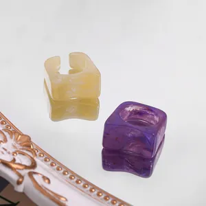 Detailed view of square marbled acrylic rings in purple and yellow on mirror surface.
