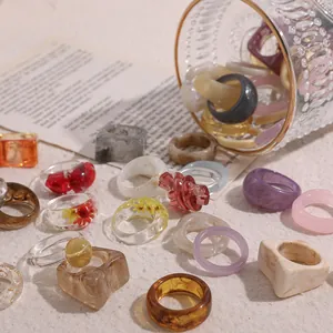 Assorted acrylic resin ring set featuring dried flowers and marble patterns on sandy background