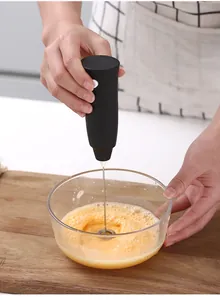 Primer plano de una mano usando un espumador de leche eléctrico para batir huevos en un tazón