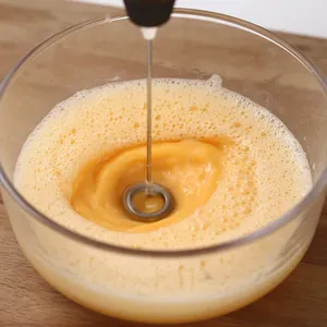Espumador de leche eléctrico portátil batiendo huevos en un cuenco de cristal transparente