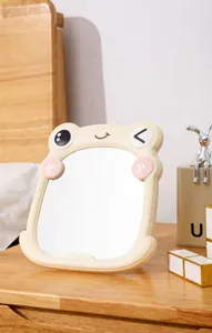 Detailed view of a cute yellow cartoon frog-shaped plastic makeup mirror on a wooden desk