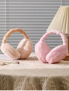Cache-oreilles en peluche rose et beige sur table douce avec lampe chaude