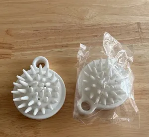 Close-up detail of a white silicone scalp massage brush showing the packaging on wooden surface