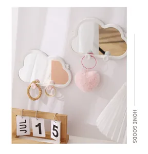 Detail of white cloud-shaped wall mirror holding pink heart keychain and hair scrunchies