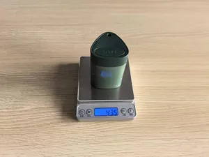Detail shot of a 43.5g green press-type plastic toothpick box weighed on a digital scale.