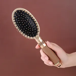 Champagne gold paddle hairbrush with air cushion held by hand against brown background