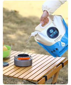 8L portable water bag pouring water into a camping kettle on a wooden table outdoors
