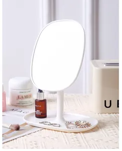 Detail view of white oval desktop makeup mirror with storage base holding jewelry