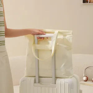Große faltbare Taslon-Reisetasche, die am Griff eines weißen Rollkoffers befestigt ist