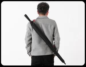 Back view of a man carrying a large black long-handle umbrella with a shoulder strap.