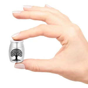 Close-up of small silver pet urn with Tree of Life engraving held between fingers