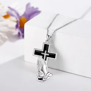 Detail of stainless steel cross memorial pendant with praying hands motif on a white block