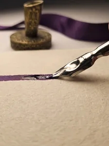 Macro detail view of vintage metal calligraphy pen nib writing with deep purple ink on paper