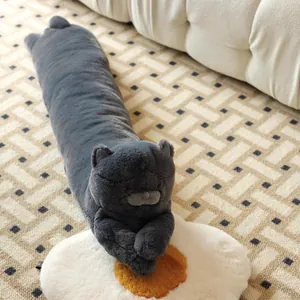 Vue détaillée d'un long coussin en peluche chat gris posé sur un tapis à motifs beige