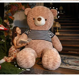 Giant light brown teddy bear plush toy wearing striped shirt in home setting