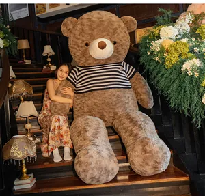 Giant brown plush teddy bear in striped shirt sitting on wooden stairs with model