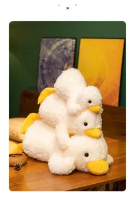 Three cute white plush duckling toys stacked on a wooden table in a warm room