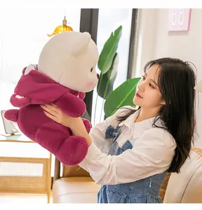 Young woman holding a plush teddy bear wearing a purple hoodie in a cozy room.