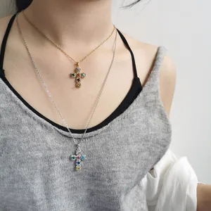 Macro detail of stylish colorful zircon cross pendant necklaces worn by a female model.