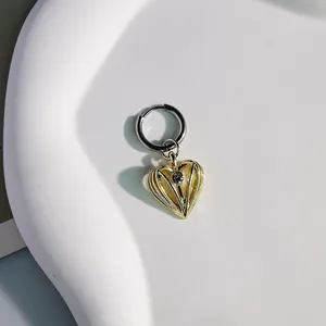 Primo piano di un ciondolo a cuore dorato su un orecchino a cerchio argento lucido
