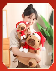 Modelo asiática sosteniendo dos peluches de carpincho navideños de diferentes tamaños