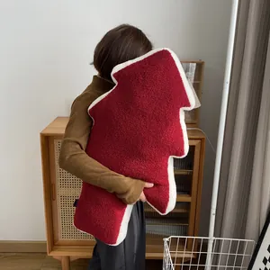 Coussin sapin de Noël en polaire Sherpa rouge tenu dans un intérieur chaleureux