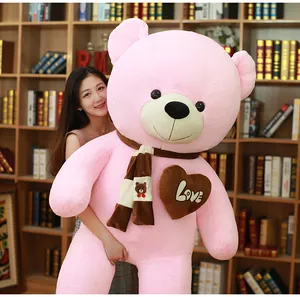 Soft giant pink plush teddy bear wearing a striped scarf and love heart patch detail.