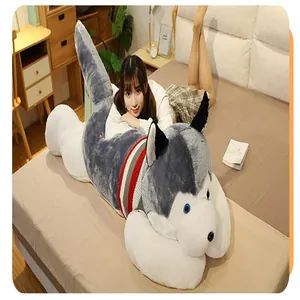 Almohada gigante de peluche de husky con modelo en cama para referencia de talla.