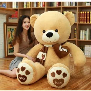 Giant brown plush teddy bear with a Love heart pillow and a cozy scarf detail