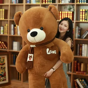 Giant brown plush teddy bear with striped scarf and heart patch held by a woman