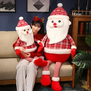 Large and medium plaid Santa Claus plush dolls in a warm living room holiday setting.