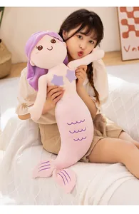 Close-up detail of soft pink mermaid plush doll being held in a cozy home setting